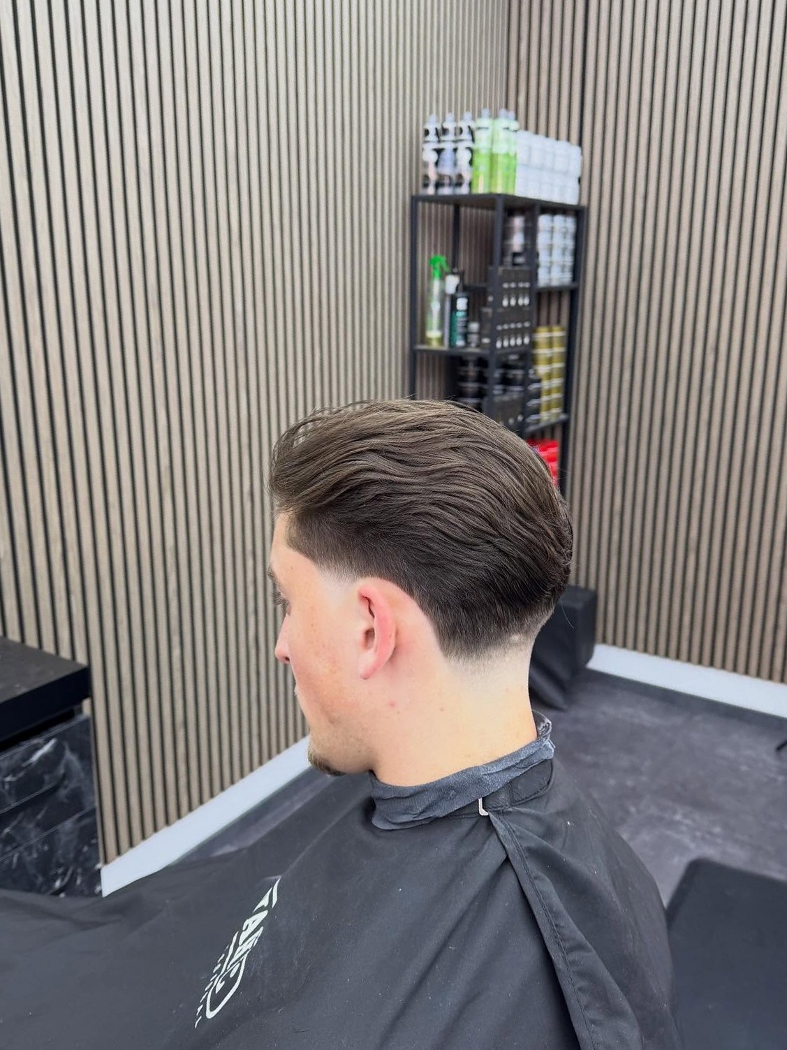 Taper fade, achterkant en zijkant, klant in de stoel voor de houten lamellenwand