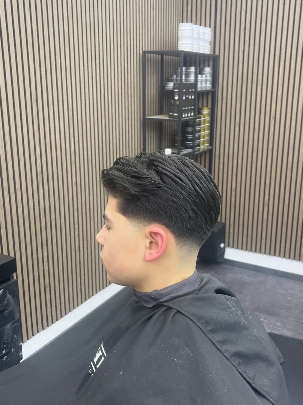 Taper fade van opzij, donker haar naar achteren, klant in de stoel